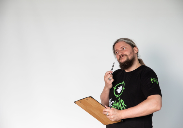 Roland Golla mit Stift am Kinn denkend hält ein Klemmbrett in der Hand